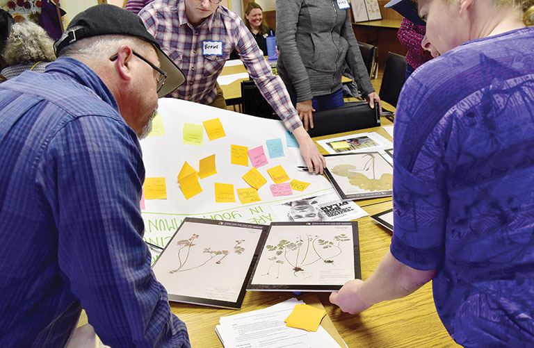 Farmers examining herbarium specimens at a table.