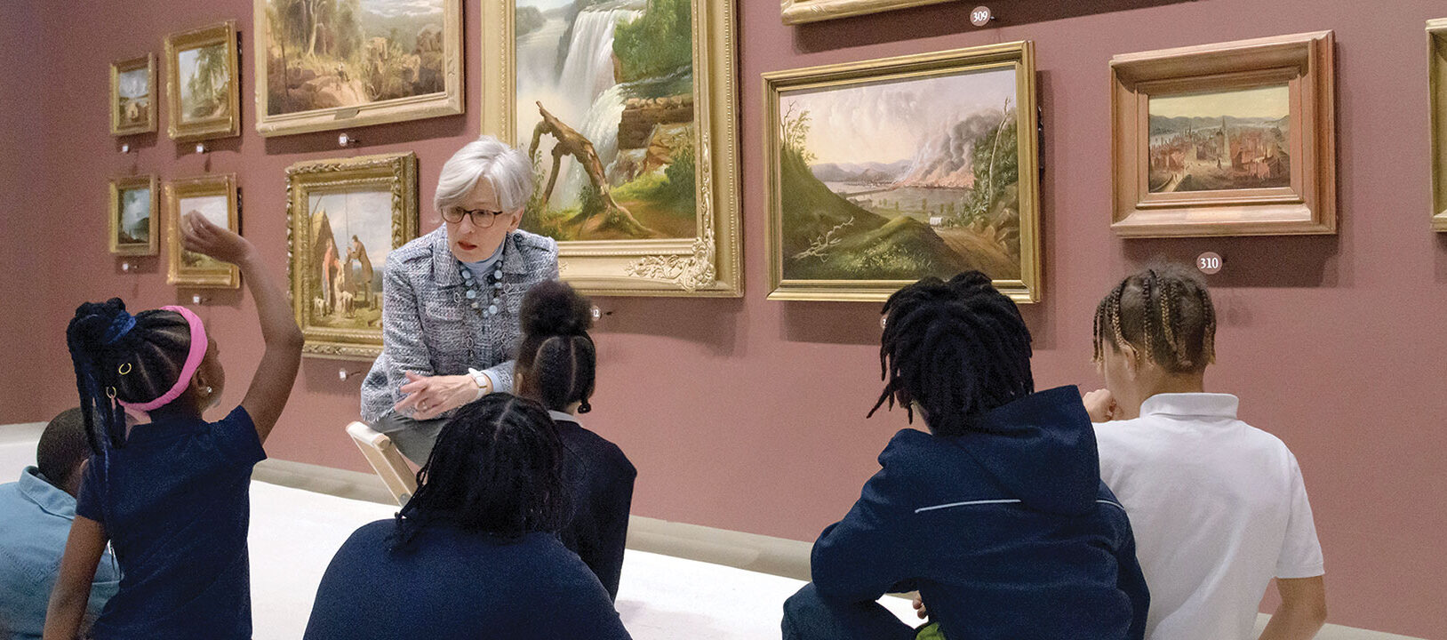 An art docent talking to a group of young students in an art gallery.