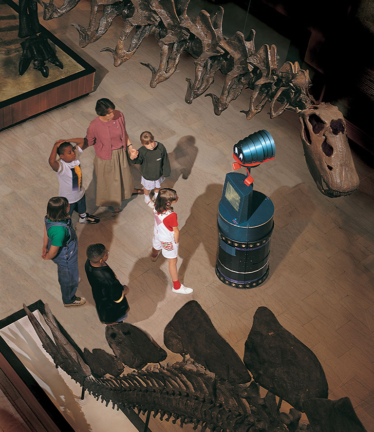 An overhead photo of a group of children standing in front of a robot