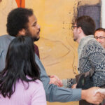 A group of museum-goers greeting each other in front of a large painting in the gallery.