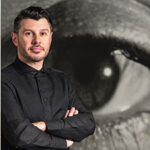 A portrait of Aaron Garvey with a large photo of a human eye behind him.