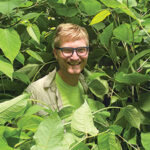 man surrounded by green plants with only his face visible.