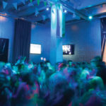 A blurred image of a group of teens dancing in the Andy Warhol Museum lobby.