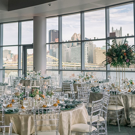 Elegant dining setup with gold and green decor, overlooking a city skyline through large windows.