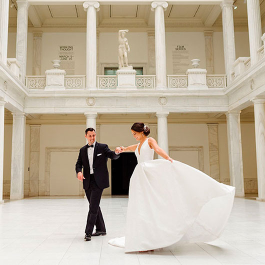 A couple dances in an elegant marble hall, the bride in a flowing white gown and the groom in a classic tuxedo.