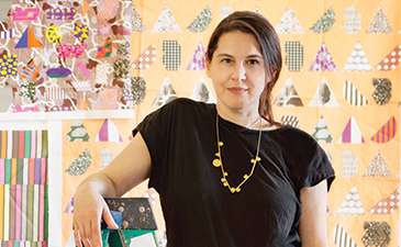ARtist Ruth Root standing on a ladder in front of digitally printed fabric swatches.