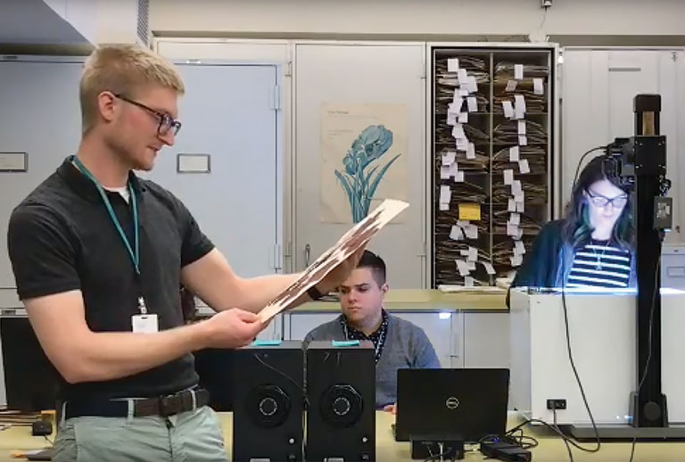 A man holding a botany specimen with young people working behind him