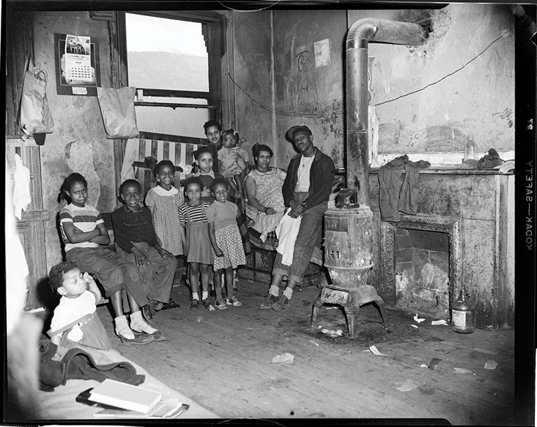 family posed in their dilapidated home with graffiti on wall inscribed “Be kind to everyone