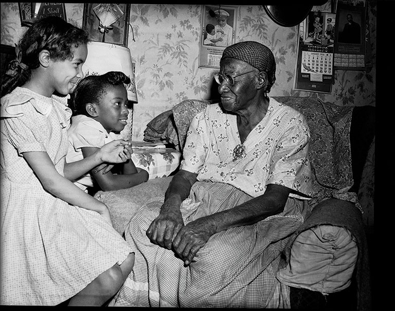 AN aged woman sitting and talking to two young girls