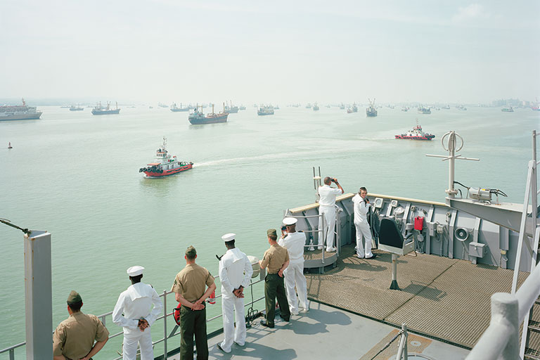 Sailors standing on teh deck of a shop looking out at other ships in the water