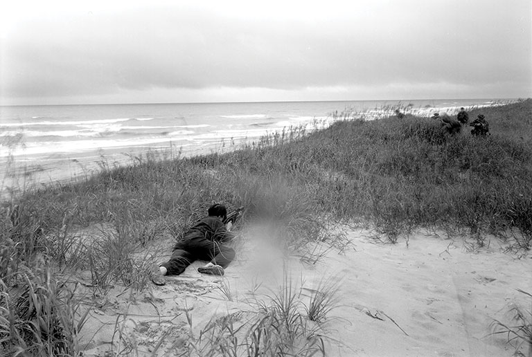 A re-enactment of a sniper crawling towards soldiers