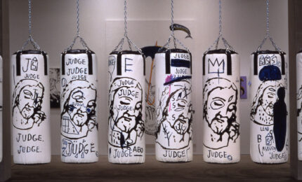 A row of 10 punching bags hanging in a gallery painted with depictions of Jesus