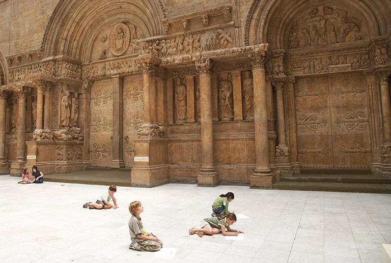 Young children drawing on the floor in front of a large structure in the hall of architecture