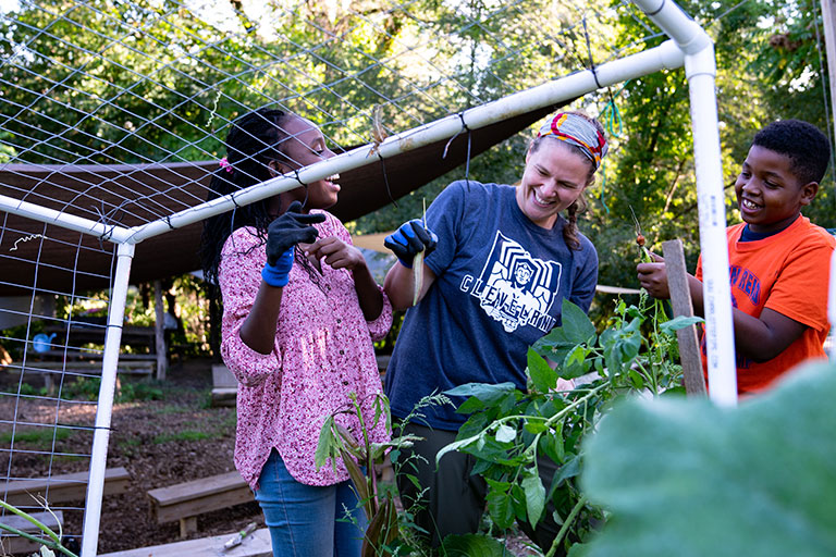 A woman and 2 children working on a community farm