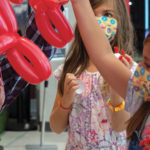 a man and 2 children holding red and blue balloons shaped like viruses
