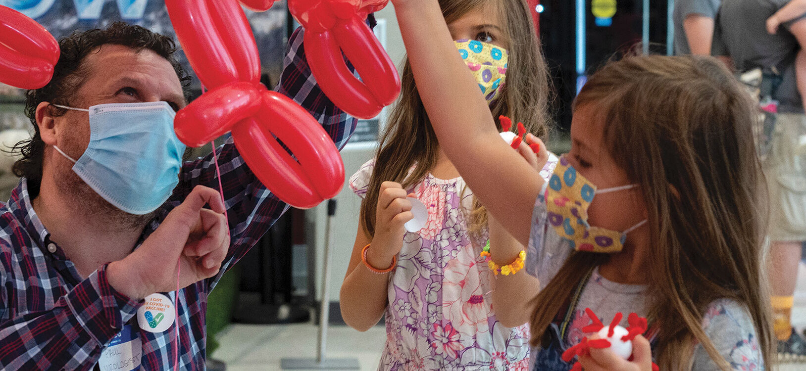 a man and 2 children holding red and blue balloons shaped like viruses