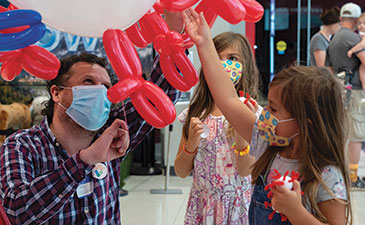 a man and 2 children holding red and blue balloons shaped like viruses