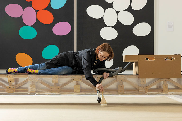 A conservator working on a piece of artwork suspended above on a bridge-like construction