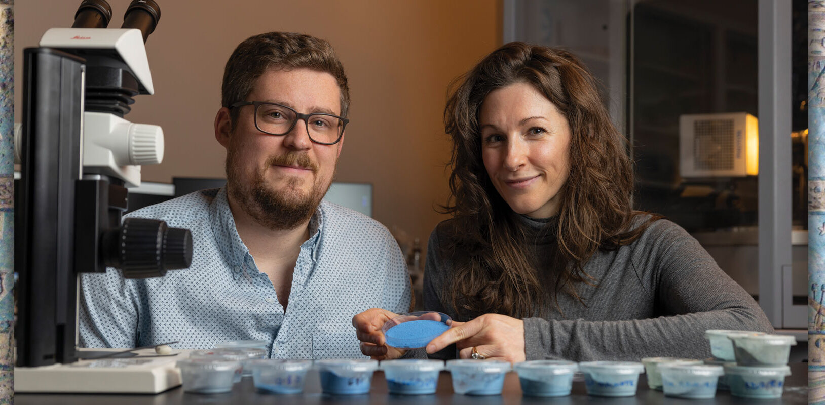 Two scientists posing with a blue powder in a petri dish