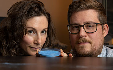 Two scientists posing with a blue powder in a petri dish