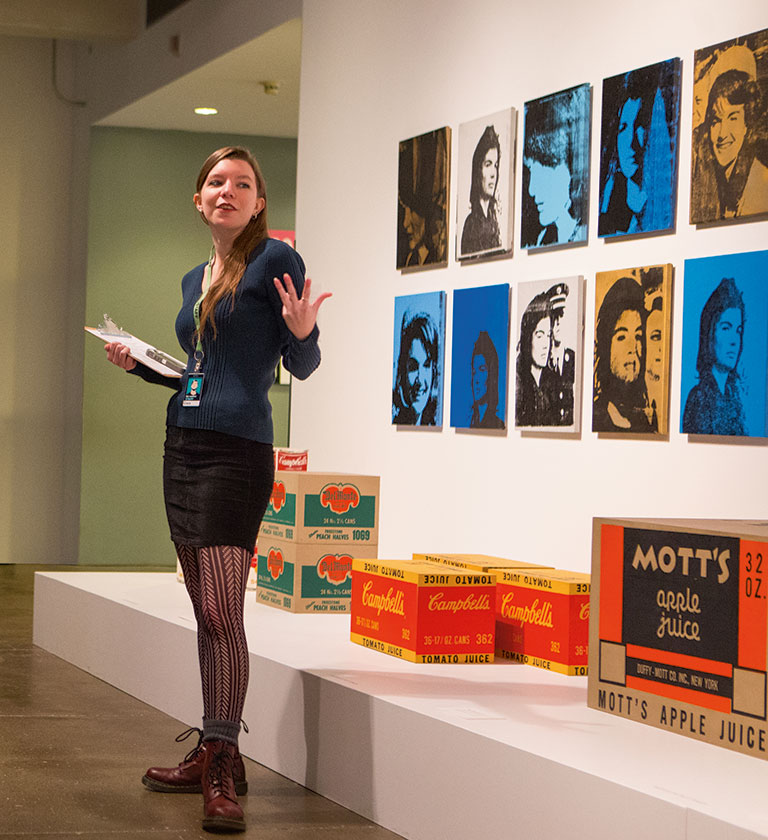 A young curator talking in front of Warhol artwork.