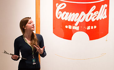A young educator standing next to a Warhol Campbells soup painting.