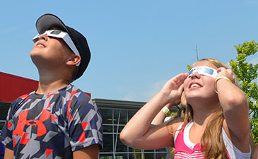 Two children staring at the solar eclipse wearing protective glasses.