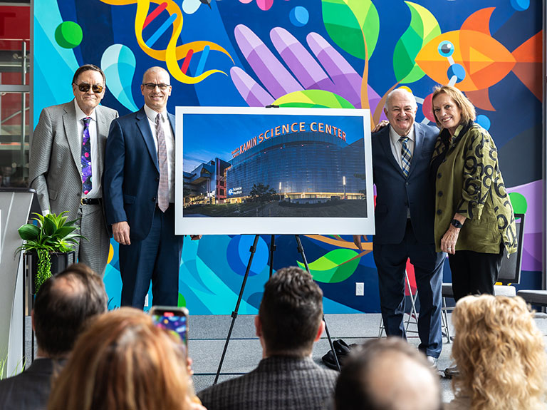 Donors and museum staff standing next to an easel with a large photo of a Science center.