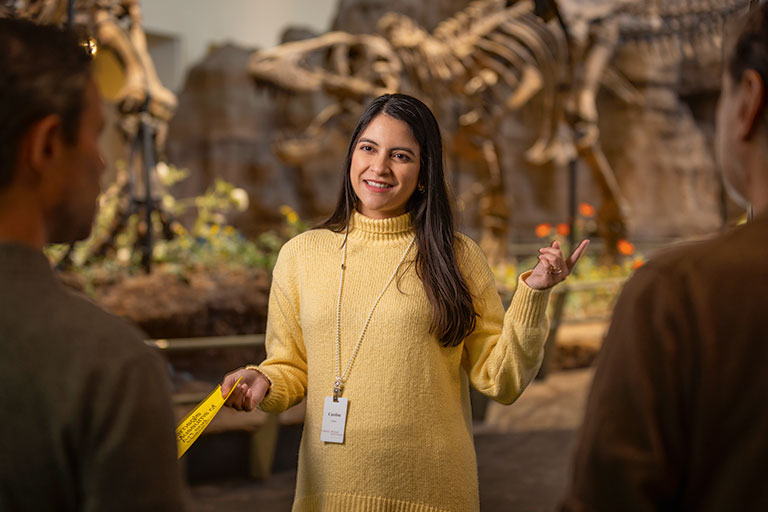 A young female volunteer talking to two men in the dinosaur exhibit.