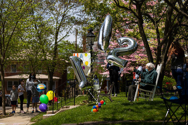AN elderly man sitting in his front yard with people waving to him.