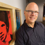 Donald Warhola standing next to portraits of himself created by his uncle Andy Warhol