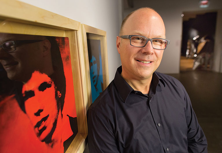 Donald Warhola standing next to portraits of himself created by his uncle Andy Warhol