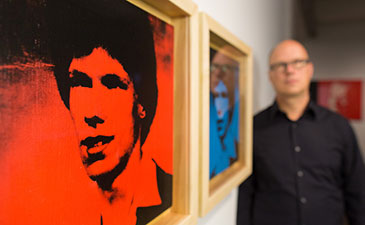 Donald Warhola standing next to portraits of himself created by his uncle Andy Warhol