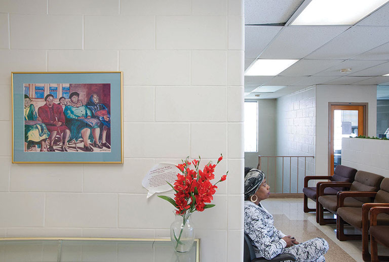 A view of a library with a paitnign on teh wall. A woman sits on a bench nearby.