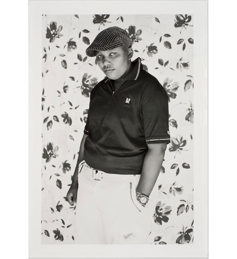 A black and white portrait of a person standing in front of flowered wallpaper