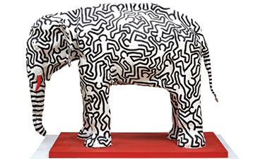 A large plaster elephant with black figures painted on it.
