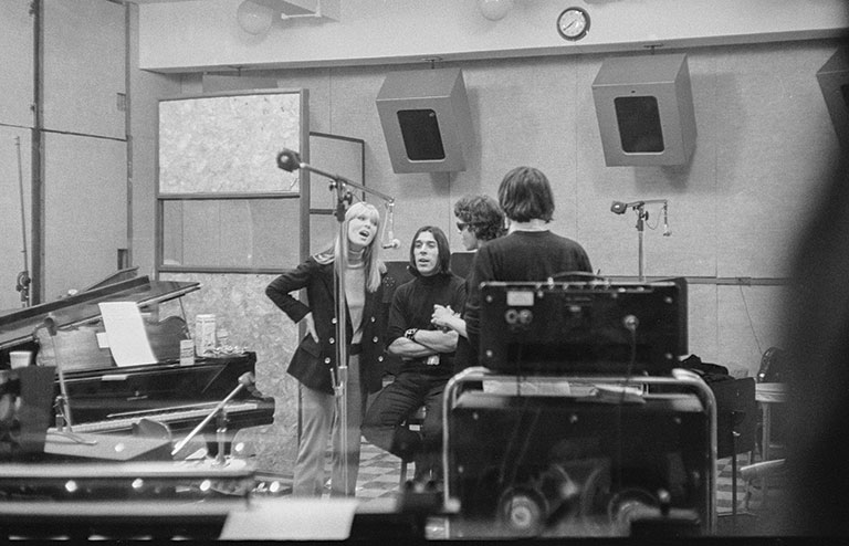 Black and white photograph of the Velvet Underground & Nico with Andy Warhol standing outside in front of a corner of a building.