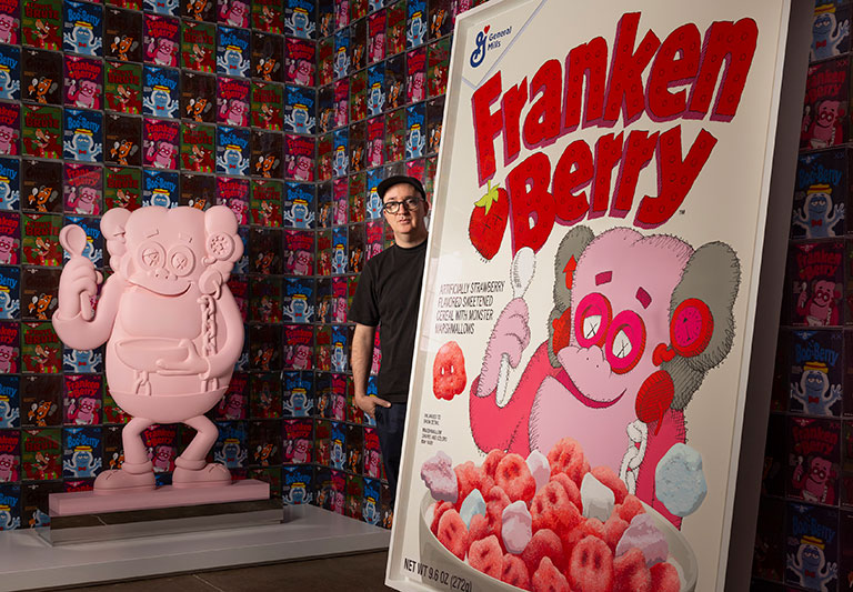 A portrait of the artist, Kaws standing among some of his work.