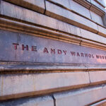 Close-up of the entrance sign for The Andy Warhol Museum, featuring textured stone and bold red lettering.