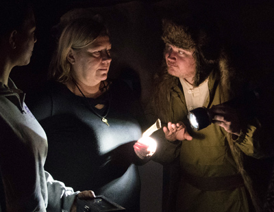 Man dressed as an arctic explorer holding a flashlight and speaking to a group in a dark room