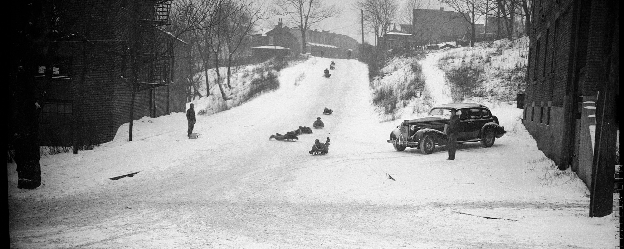 vintage black and white photo of kids sled riding down a street