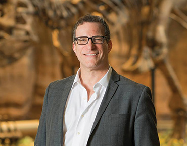 A portrait of Eric Dorfman standing in the Dinosaur exhibit.