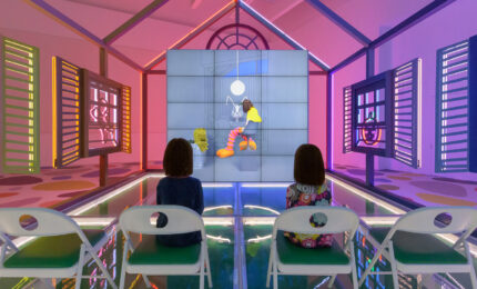 Two young girls sitting in chairs inside a neon house watching a video.