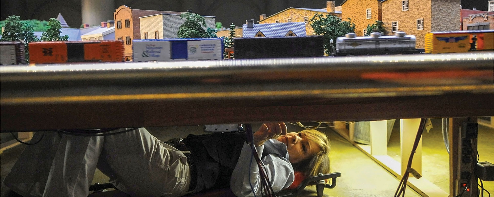 Woman working underneath a model train platform.