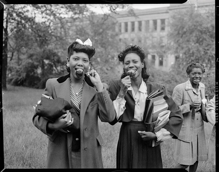 A black and white photo of two African-American girls eating candy apples.