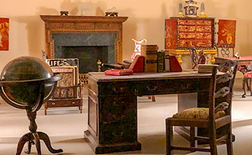 A miniature version of a room with a desk, glaobe and magazine rack.