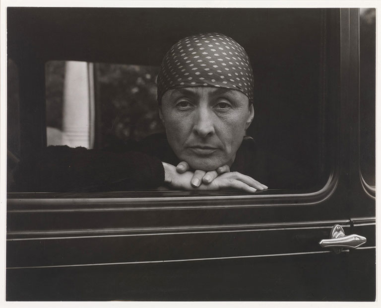A black and white photo of a Georgia Okeeffe sitting in a vintage automobile