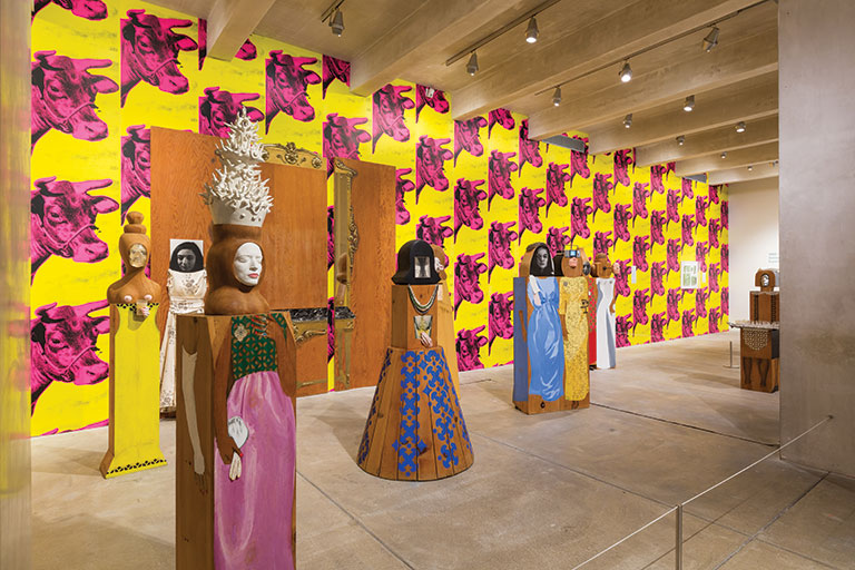 An art exhibit showing figures in front of a cow patterned wallpaper wall