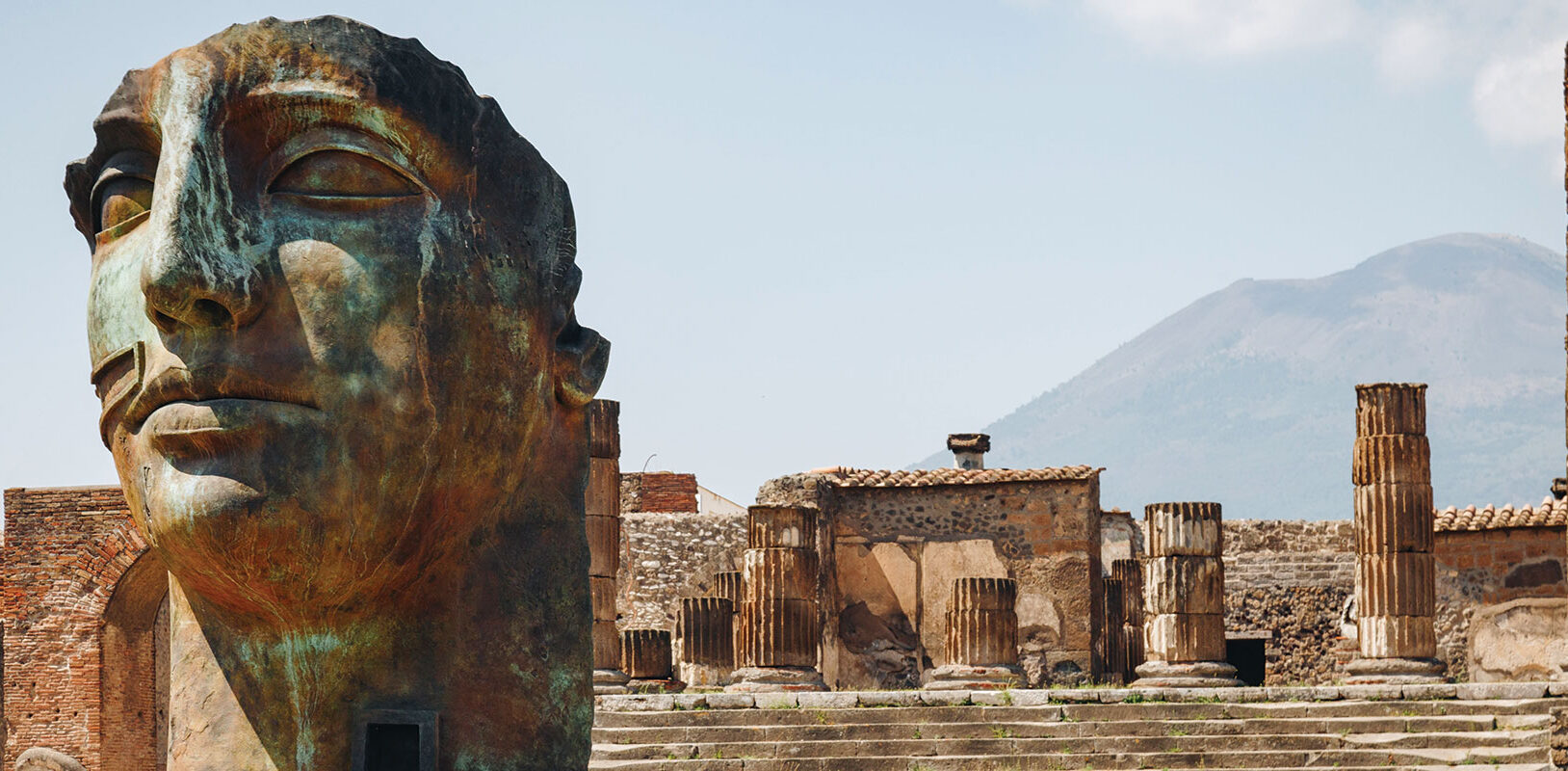 A few of a city ruins with a large sculpture of a human face in the foreground