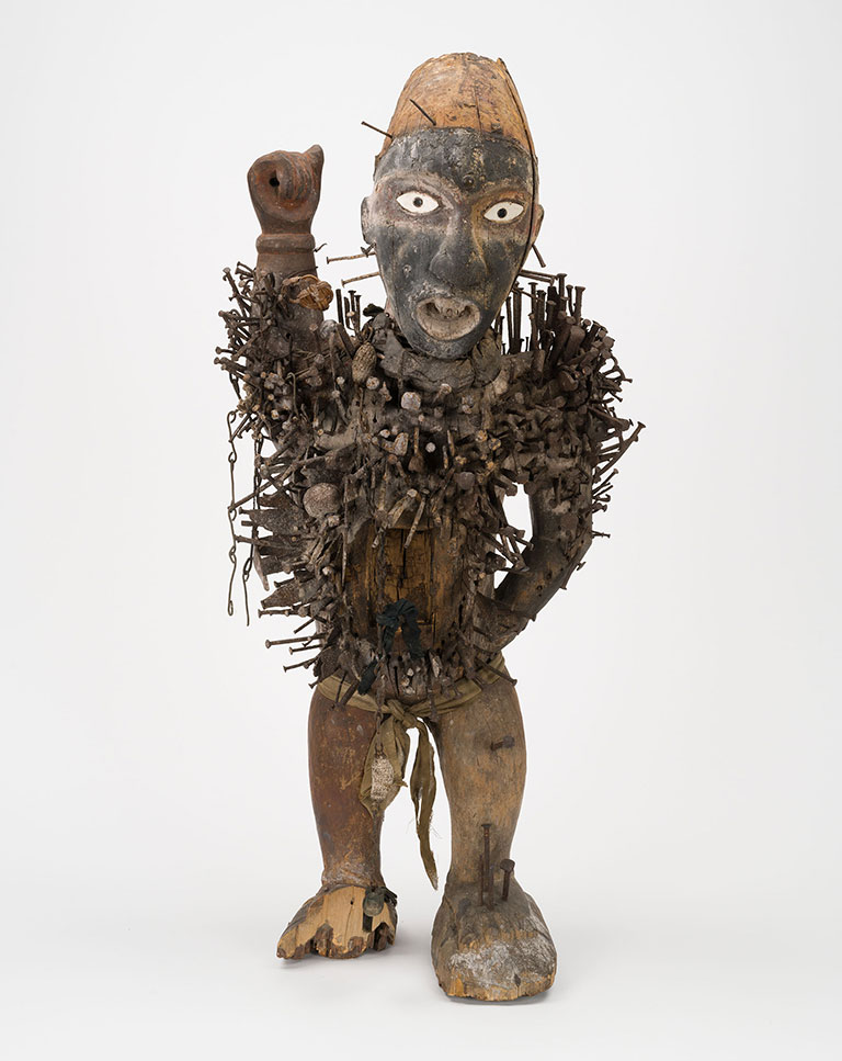 A primitive wooden sculture with nails protruding from it